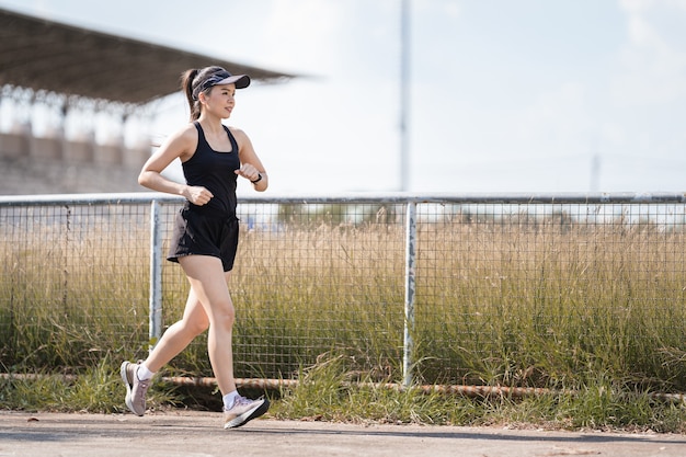 A healthy happy Asian woman runner in black sport outfits jogging in the natural city park under evening sunset