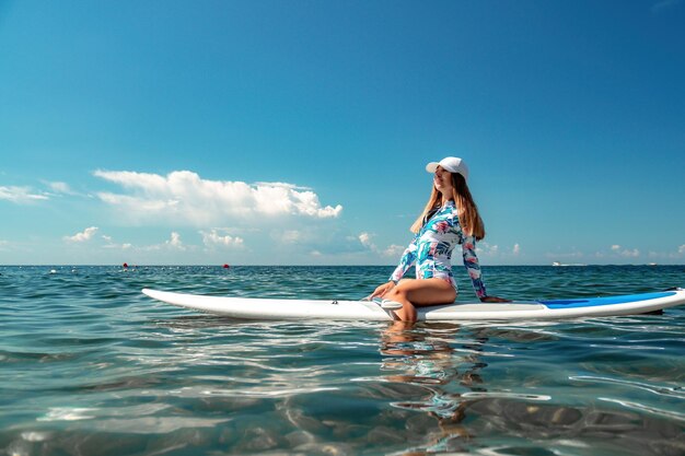 Healthy happy fit woman in bikini relaxing on a sup surfboard floating on the clear turquoise sea