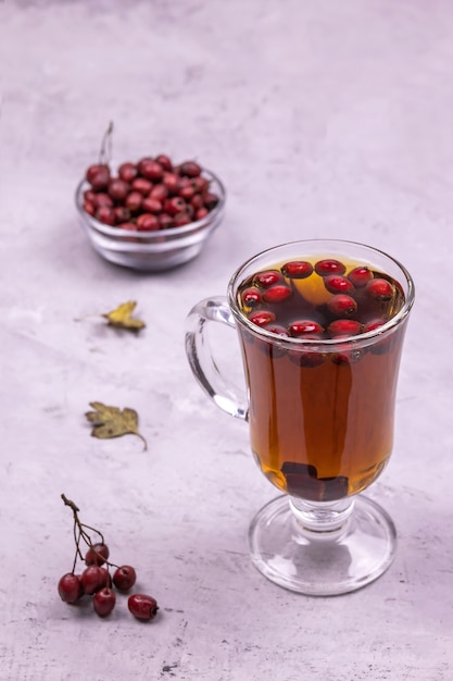 Healthy hawthorn berry tea in a glass and a handful of berries in a glass bow