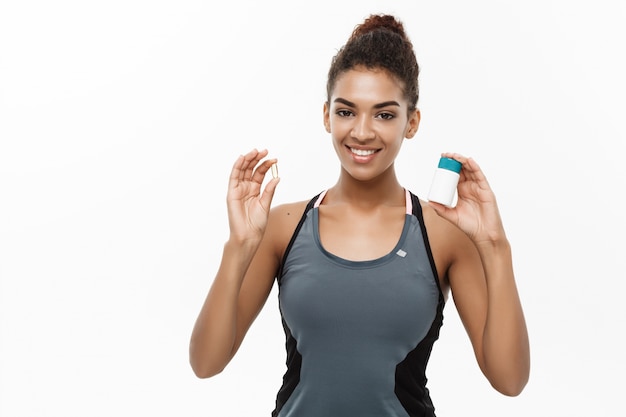 Healthy and healthcare concept - portrait of beautiful sporty African American holding bottle of supplementary bottle. Isolated on white studio background.