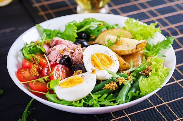 Healthy hearty salad of tuna, green beans, tomatoes, eggs, potatoes, black olives close-up in a bowl on the table. 