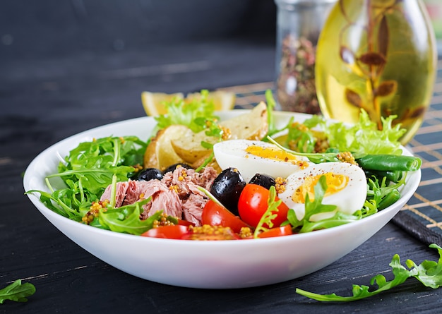 Healthy hearty salad of tuna, green beans, tomatoes, eggs, potatoes, black olives close-up in a bowl on the table. 