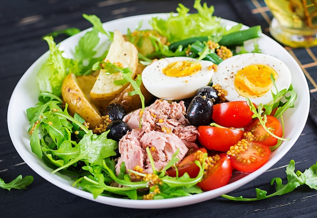 Healthy hearty salad of tuna, green beans, tomatoes, eggs, potatoes, black olives close-up in a bowl on the table. 