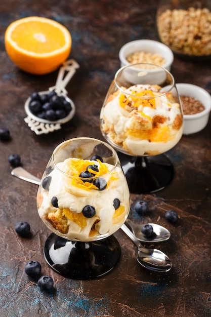 Healthy homemade layered dessert trifle with orange, blueberry, biscuit, yogurt and granola in a glasses