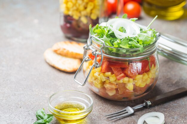 Insalata di verdure fatta in casa in un barattolo di muratore sano con pomodori, mais, pepe, rucola e cipolla