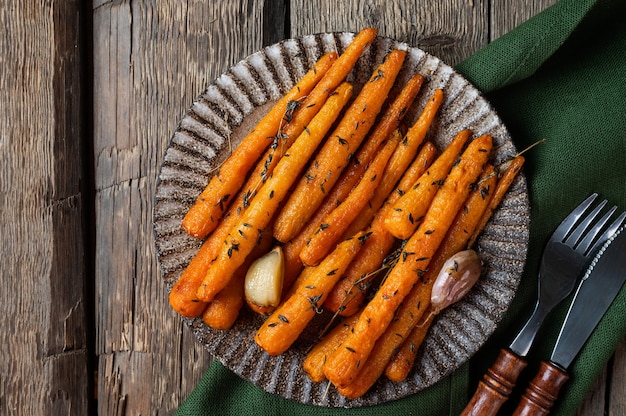 Healthy homemade roasted carrots ready to eat. glazed carrot\
with herbs and garlic top view. fried carrot on wooden background.\
sauteed vegetables. comfort food.