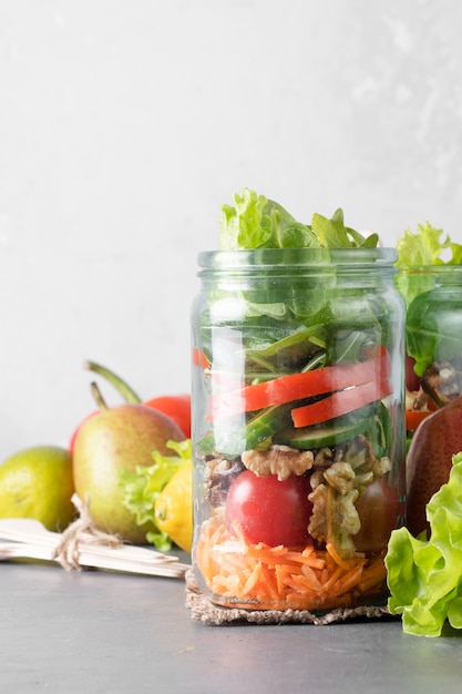 Healthy homemade salad with fresh pear, tomatoes, carrots and herbs in jars