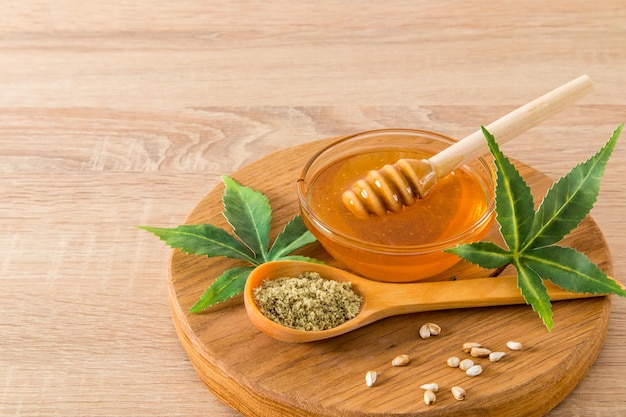 Healthy honey with cannabis products in a bowl on a round wooden board ground and whole seeds of morejuana Front view wooden background