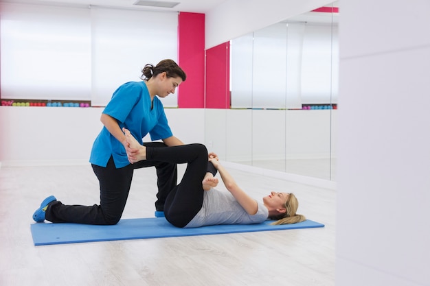 Healthy instructor stretching patient legs at the gym