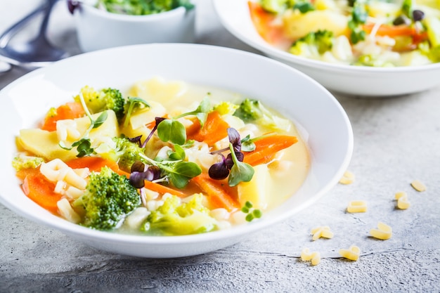 Healthy kids alphabet soup with broccoli, carrot and potato in white plates.