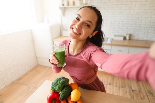 Signora in buona salute che fa selfie con frullato verde dopo l'allenamento al coperto