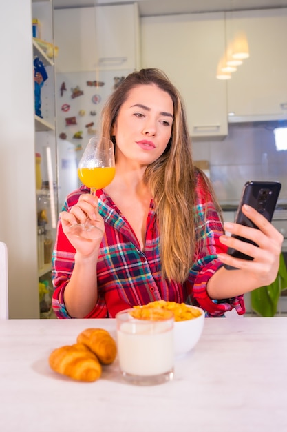 Healthy lifestyle, blond Caucasian woman with orange juice for breakfast and taking a selfie with mobile phone