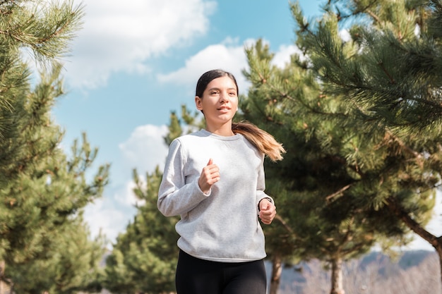 Healthy lifestyle. cheerful attractive woman running in park with pine trees in the morning