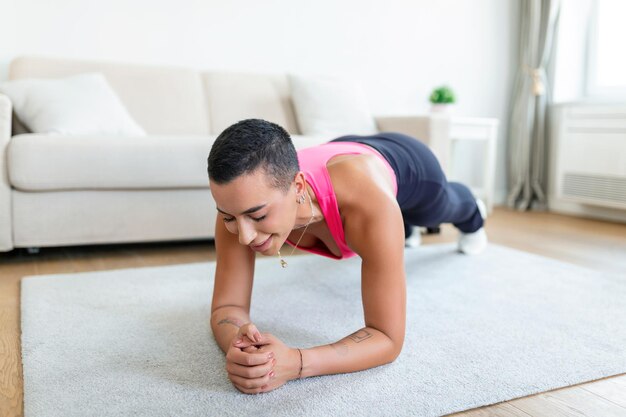 Concetto di stile di vita sano donna afroamericana in piedi nella posizione della plancia sul tappetino da yoga a casa o in studio fitness donna allegra in abbigliamento sportivo allenamento core e muscoli addominali