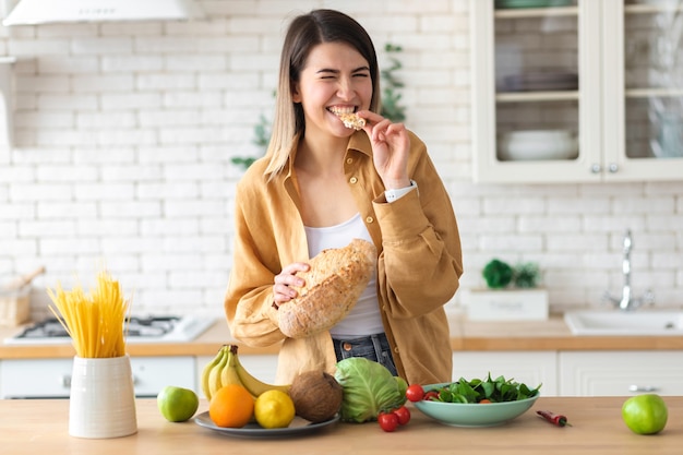 健康的なライフスタイルのコンセプト。健康的な栄養のための食品のセットを持つ美しい若い女性は、台所で家に立っています