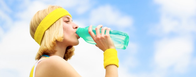 Healthy lifestyle concept. Drinking during sport. Young woman drinking water after run. Woman in sports wear is holding a bottle of water. Sports girl drinks water from a bottle on a sky background.