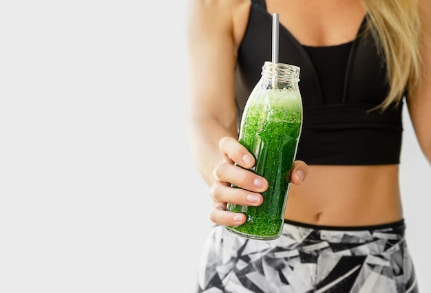 Concetto di stile di vita sano. donna di forma fisica che tiene una bottiglia di broccoli e frullato di spinaci.