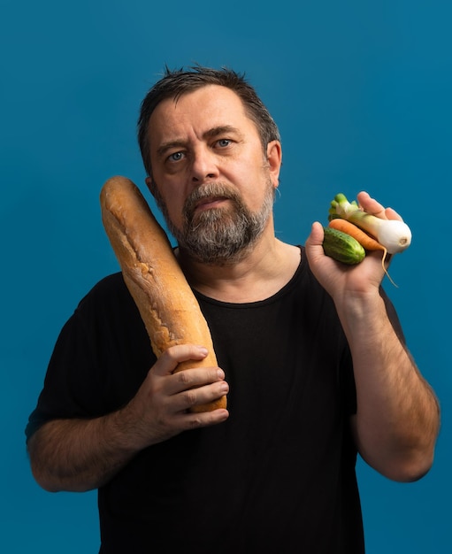 Концепция здорового образа жизни. Трудный выбор. Что лучше хлеб или овощи. Мужчина средних лет в черной футболке держит в одной руке яблоко, а в другой - хлеб.