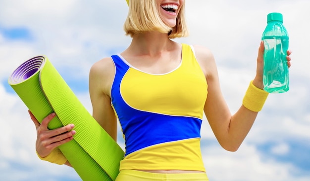 Healthy lifestyle concept. Woman in sports wear is holding a yoga mat and bottle