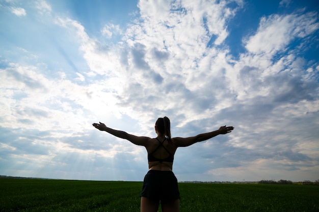 Healthy lifestyle concept. Young attractive woman in sportswear does stretching her hand before training on the nature against a blue sky. Muscle warming