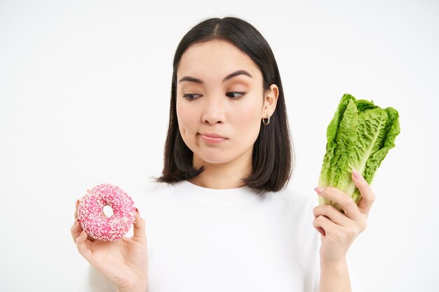Фото Концепция здорового образа жизни молодая женщина выбирает между здоровой овощной капустой и вкусной глазурью