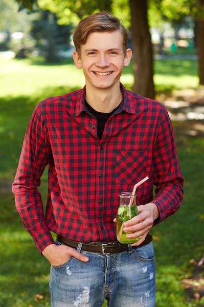 Healthy lifestyle. Happy young man with detox cocktail in summer, on green nature background