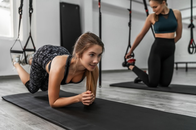 Healthy lifestyle. Portrait of young sportive girl doing plank with trx fitness straps in the gym