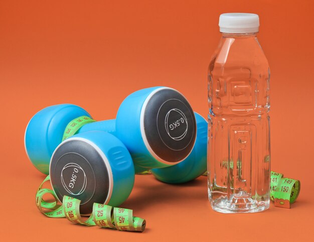 Healthy lifestyle still life. Dumbbells, ruler,  bottle of water on orange