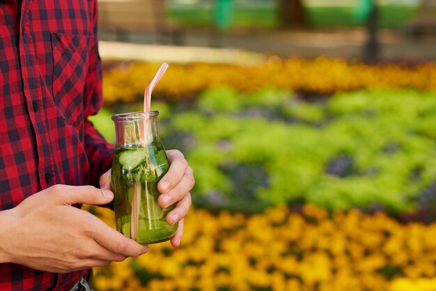 Healthy lifestyle. Unrecognizable young man with detox cocktail in summer, on green nature background. Diet, well being and weight loss concept