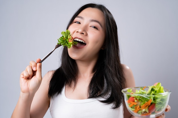 Healthy lifestyle with Clean food concept. Happy asian woman eating salad isolated over white wall.