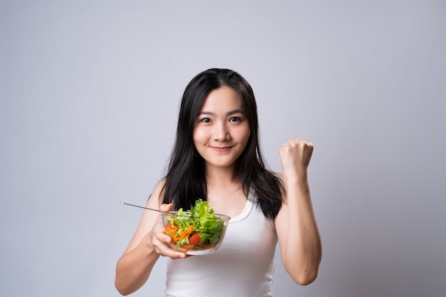 Healthy lifestyle with Clean food concept. Happy asian woman eating salad isolated over white wall.