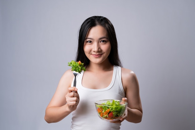 Healthy lifestyle with Clean food concept. Happy asian woman eating salad isolated over white wall.