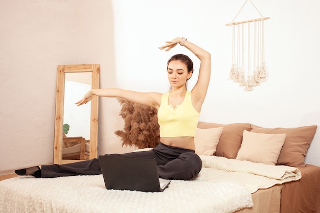Здоровый образ жизни. Женщина на кровати. Утренняя зарядка онлайн с ноутбуком.