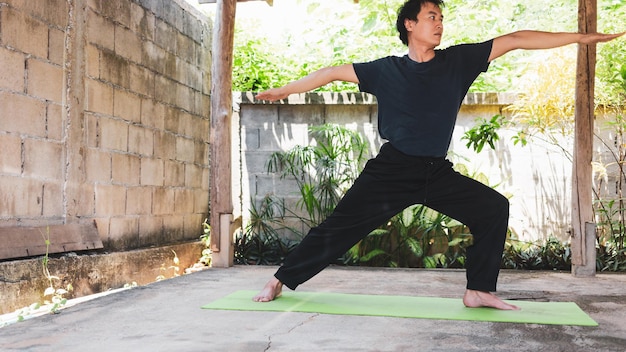 Concetto di vita sana di giovane uomo asiatico che pratica yoga asana guerriero in piedi posa