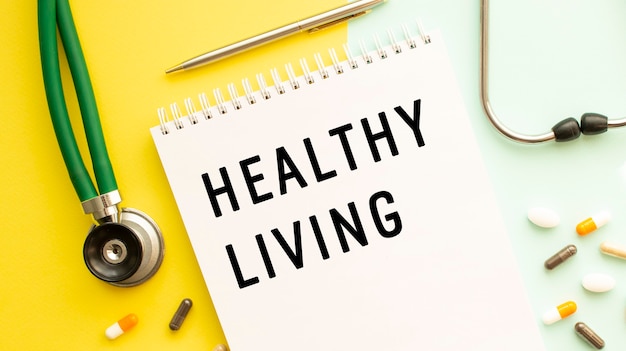 HEALTHY LIVINGは、丸薬と聴診器の横にあるカラーテーブルのノートに書かれています。医療コンセプト