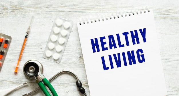 HEALTHY LIVINGは、錠剤と聴診器の横にある白いテーブルのノートに書かれています