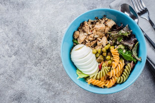 Healthy lunch bowl. Chicken, pasta fusilli, mix greens, green peas on concrete background