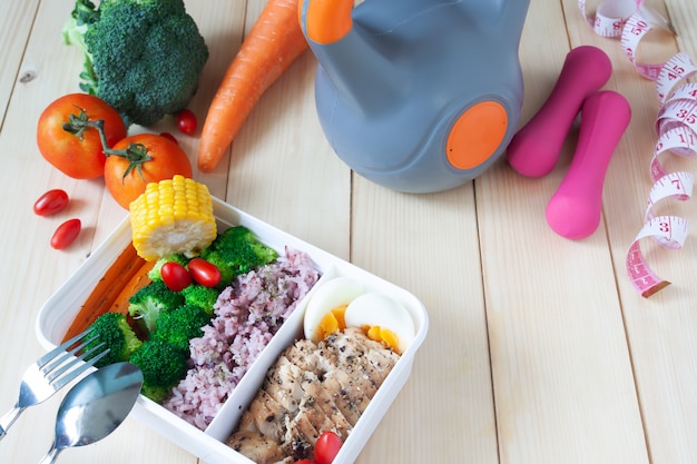 Healthy lunch box with sport and fitness equipments on wooden background