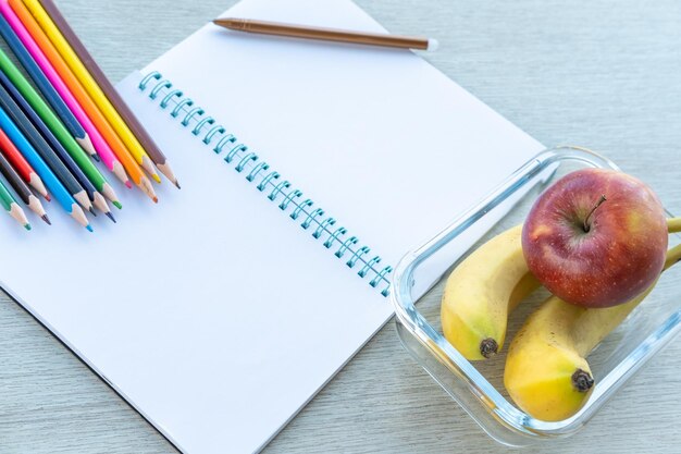 A healthy lunch in a glass container an open empty notebook pen pencils school supplies Back to school