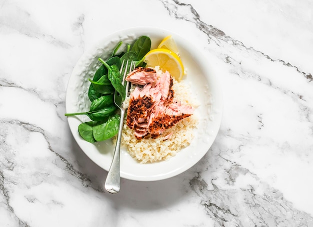 Здоровый обед с лимонным кускусом, жареным лососем и свежим шпинатом на светлом мраморном фоне, вид сверху