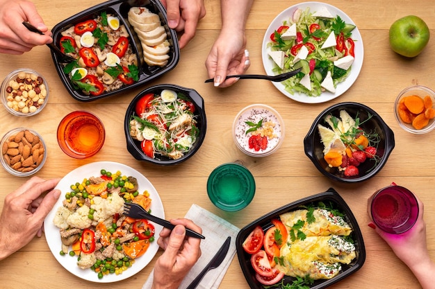 healthy lunch time at office workplace. four people eating healthy meals from take away lunch boxes and plates at wooden table. concept, top view