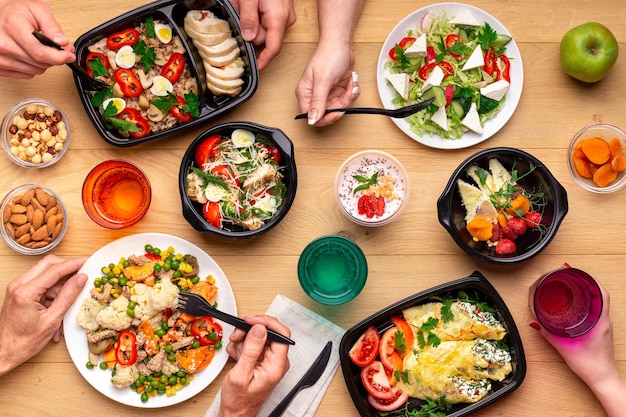 Healthy lunch time at office workplace. Four people eating healthy meals from take away lunch boxes and plates at wooden table. concept, top view