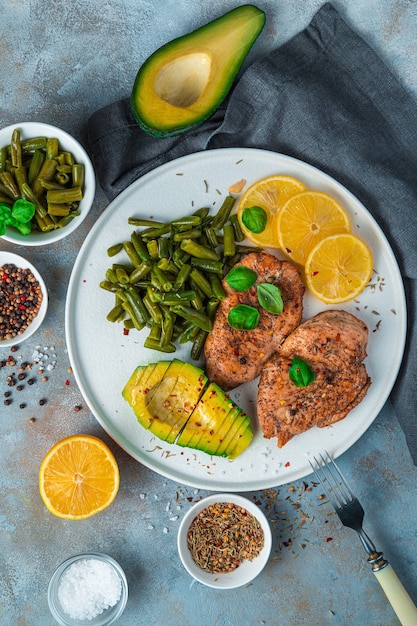 Healthy lunch with avocado, chicken breast and beans on a gray background.