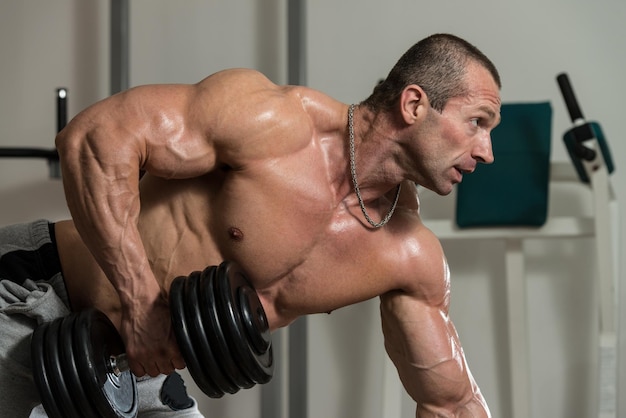 Healthy Man Doing Back Exercises In The Gym With Dumbbell