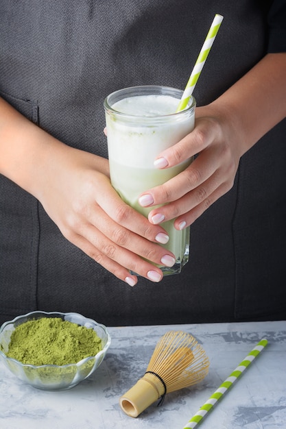 A healthy matcha drink. The barista girl is holding a glass of green tea latte in her hands.