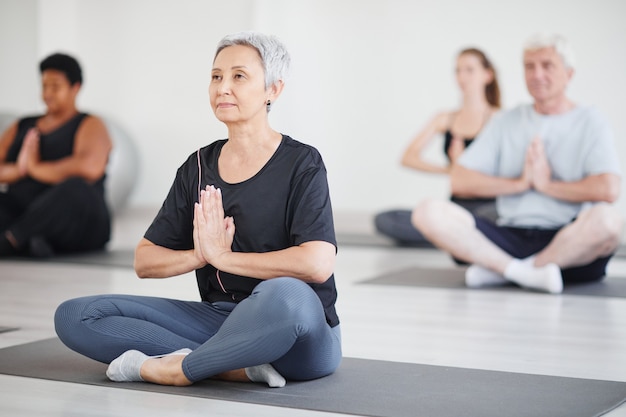 Photo healthy mature woman sitting on exercise mat in lotus position and doing yoga in the class