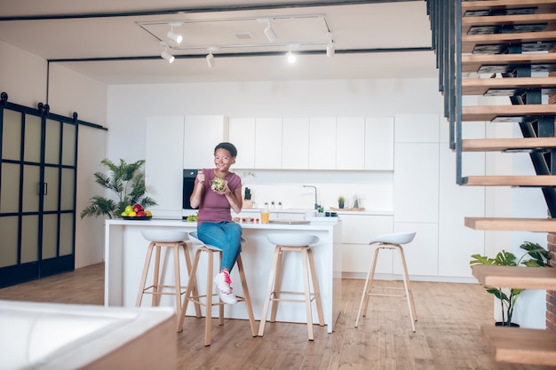 Healthy meal. A dark-skinned woman sitting in the kitchen and eating salad