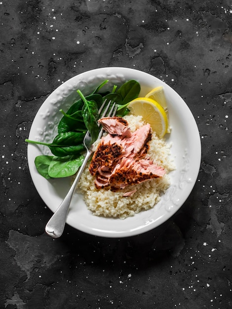 Здоровый средиземноморский обед с лимонным кускусом, жареным лососем и свежим шпинатом на темном фоне, вид сверху