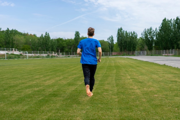 Healthy morning running, male athlete on the green grass fields with bare feet