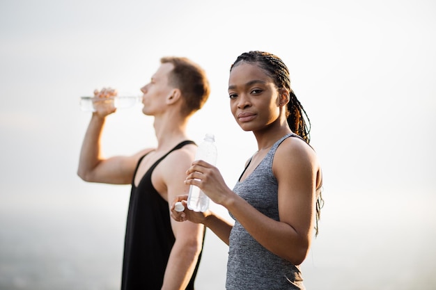 Здоровая мультикультурная пара пьет воду после тренировки